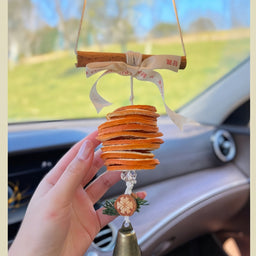 Close-up of car hanging ornament with dried orange slices, ribbon bow, and bell