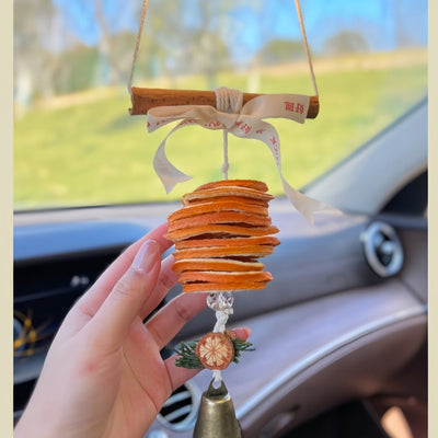 Close-up of car hanging ornament with dried orange slices, ribbon bow, and bell