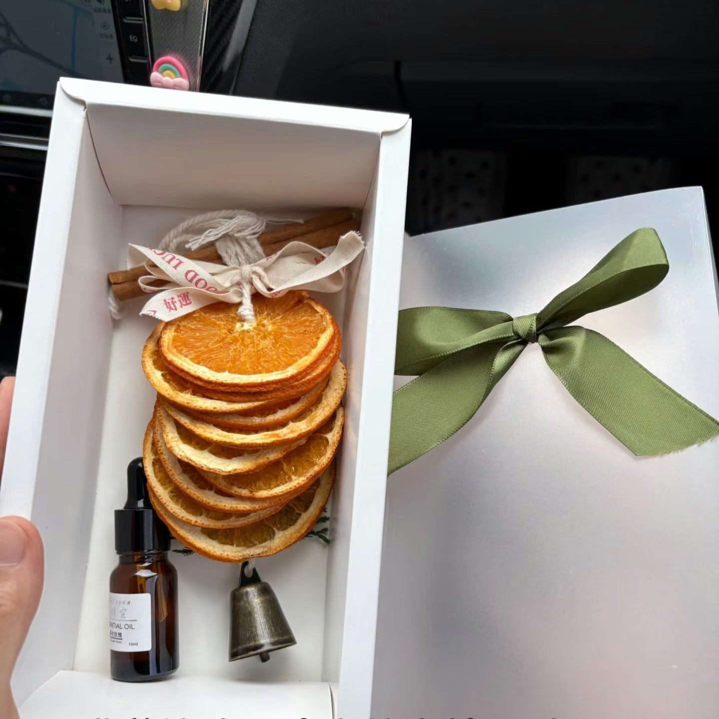 Gift set with dried orange slices, essential oil bottle, ribbon bow, and bell in a white box