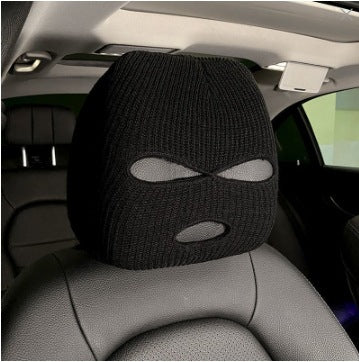 Black knitted car headrest cover with eye-shaped cutout design, installed on a car seat in the interior